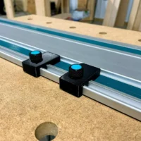 Two black 3D-printed limit stops mounted on a Makita track saw rail with blue knurled knobs for adjustment