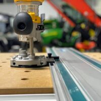 Dewalt DNP612 router adapter mounted on Makita guide rail, showing black wheel and metal base connected to the track