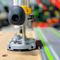 Black guide rail adapter mounted on a Dewalt trim router base, positioned on a Festool track with green edge guide stripe