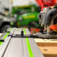 Milwaukee trim plunge router mounted on FS rail system with ToolCurve LR32 adapter plate and spring-loaded positioning knob engaged on wooden workpiece