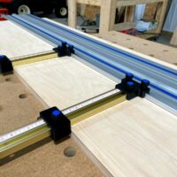 Black plastic parallel guide brackets with blue knobs mounted on brass rails attached to a Kreg ACS track saw guide rail system