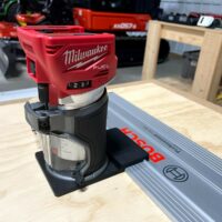 Milwaukee M18 trim router mounted on black adapter base sitting on a Bosch guide rail