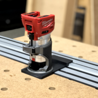 Black router base adapter mounting a Milwaukee M18 Fuel trim router to a DeWalt track on an MFT bench