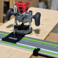 Milwaukee plunge router mounted on black ToolCurve LR32 base adapter positioned on Festool aluminum track rail with green stripe, shown on wooden workbench