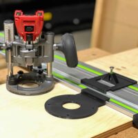 Milwaukee plunge router on LR32 rail adapter with black hole drilling plate, guide stops, and spring-loaded knob on wooden workbench