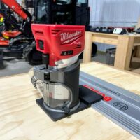 Milwaukee M18 trim router mounted on black plastic adapter base, positioned on Mafell aluminum guide rail