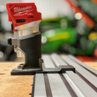 Milwaukee Fuel router mounted on black adapter seated on Dewalt track saw track, showing the red battery head and metal base plate in side view