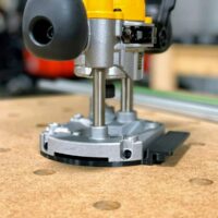 Dewalt plunge router DNP612 base with ToolCurve guide rail adapter mounted on wood workbench near reference holes