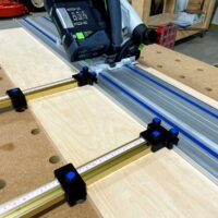 Black plastic parallel guide clamps mounted on Kreg ACS rail system with track saw positioned above wooden workpiece