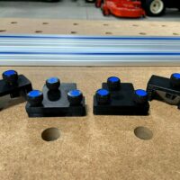 Four black 3D-printed adapters with blue knurled knobs on a perforated workbench surface, positioned above a Kreg guide rail
