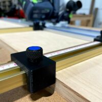Black 3D-printed parallel guide bracket mounted on Kreg guide rail with blue knurled adjustment knob and measurement scale visible