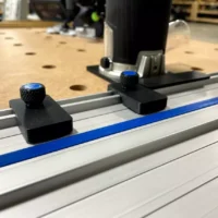 Two black limit stops with blue knurled knobs mounted on a Kreg ACS track saw guide rail, foreground and background positions