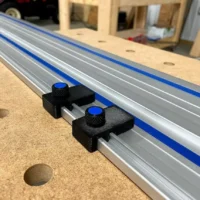 Two black limit stops with blue knurled knobs mounted on a Kreg ACS track saw guide rail