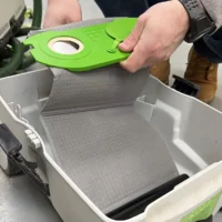 Bright green reusable filter bag held above a white Festool dust extractor container, showing the bag's curved shape and central mounting port