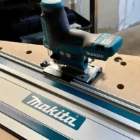 Makita 12v jig saw mounted on a Makita guide rail, showing the black adapter base connecting the saw to the aluminum rail track