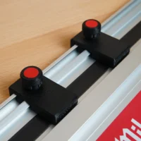Two black limit stops with red-capped knurled knobs mounted in the slot of a Milwaukee guide rail