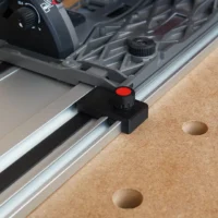 Black limit stop with red knob mounted on Milwaukee guide rail, shown attached to track saw fence on cork workbench