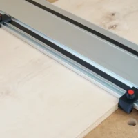 Two black drop stops with red knobs mounted on a Milwaukee track saw guide rail positioned at workpiece edges