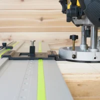 LR 32 hole drilling system mounted on a DeWalt 625 router positioned over a track saw rail, showing the plunge base plate and spring-loaded knob with guide rail stops