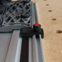 Black limit stop with red knurled knob clipped onto a Milwaukee aluminum guide rail, positioned over a pegboard workbench
