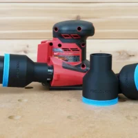 Black 2-1/2 inch hose adapter with blue trim connecting a vacuum hose to a Milwaukee 18v sheet sander, plus spare