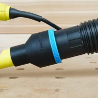 Black ToolCurve 2-1/2 inch hose adapter with blue ring joining a ribbed vacuum hose to a yellow Ryobi sander