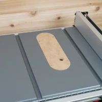 Uncut MDF Dado zero clearance insert seated in a Milwaukee M18 table saw top, screw holes and finger hole visible