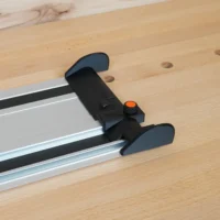 Black hose deflector with orange-topped clamping knob mounted across a PowerTec aluminum guide rail on a workbench
