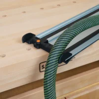 Black hose deflector mounted on a Powertec track saw guide rail, with green braided hose routed through it and an orange adjustment knob visible