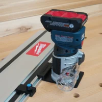 Bosch Colt 18v router mounted on a guide rail adapter, positioned on a track saw rail with holes visible on the workpiece