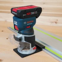 Black guide rail adapter base mounted under a Bosch GKF18V-25 Colt router, riding a track saw guide rail