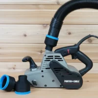 Black 2-1/2 inch hose adapter with blue trim installed on a Porter Cable belt sander, two spare adapters beside it