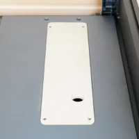 White zero clearance insert mounted in gray table saw top with four screw holes and center blade opening