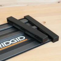 Two black PETG protective end caps slid onto the end of a Ridgid track saw guide rail on a wood bench