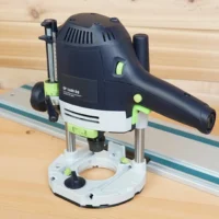 Festool OF 1400 EQ plunge router fitted with a white guide rail adapter base, sitting beside a guide rail