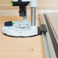 White guide rail adapter mounted on Festool 1400 router, positioned against Festool track saw rail on wood workbench