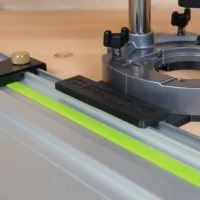 Black adapter mounted on Festool guide rail, connected to Makita router base with brass leveling knob visible on left