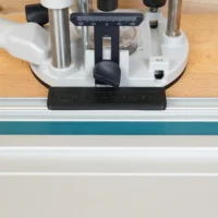 Guide rail adapter for Festool OF 1010 router mounted on a track saw rail, showing the white base with black knob and measurement scale