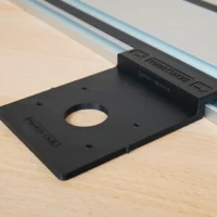 Black Rail Adapter for Porter Cable Trim Router mounted on an aluminum guide rail, shown from above on a wooden workbench