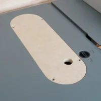 Cream MDF zero clearance insert for Craftsman CMX 10" table saw, showing oval shape with center blade slot and mounting holes, positioned on gray saw table