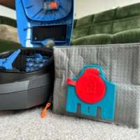 Macam reusable dust bag with red cap and grid pattern mounted on blue backing, displayed next to Miele vacuum