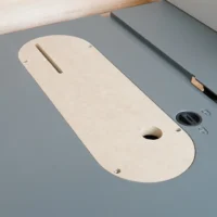 Cream-colored MDF zero clearance insert with slot and mounting holes, installed on a Craftsman table saw with gray top