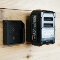 Black plastic battery mount holder installed on wood wall next to a Makita 40v Max XGT battery