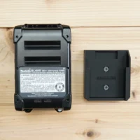 Makita 40v Max XGT battery next to a black plastic wall mount holder showing the slot designed to hold the battery