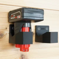 Milwaukee 12v battery mounted in black plastic holder with red battery contacts visible, shown installed on pine wood alongside an unmounted matching holder