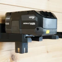 Black plastic battery holder mount with a Ryobi 18v battery clicked into place, mounted on wooden wall studs