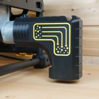 Black plastic dust collection adapter with yellow flow diagram mounted on a DeWalt table saw rear port, showing bucket hanging bracket design