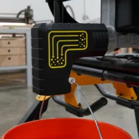 Black plastic bucket adapter with yellow ToolCurve logo attached to DeWalt table saw dust port, with red collection bucket hanging below