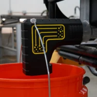 Black bucket adapter with yellow airflow graphic on a DeWalt table saw rear dust port, orange bucket hung below