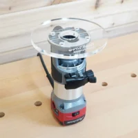 Clear 6-inch round acrylic router base plate with ToolCurve logo mounted upside down on an Avid Power trim router